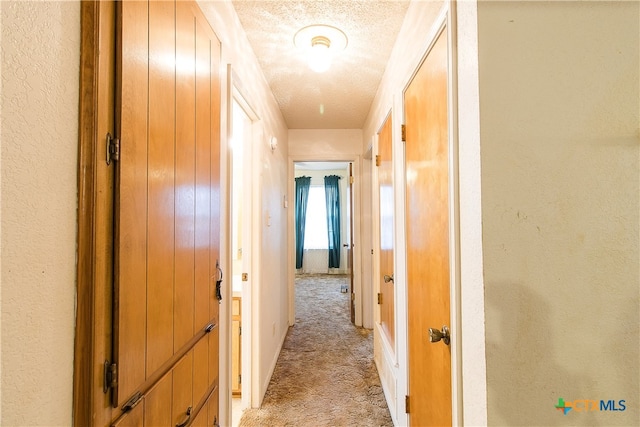 hall with a textured ceiling and light carpet