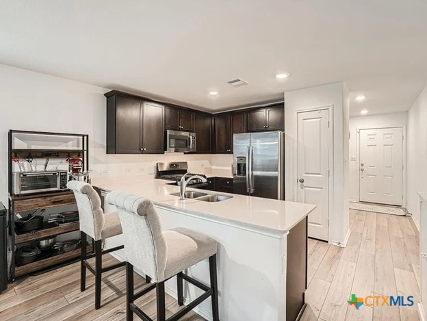 13517 Knights Branch Dr, Elgin, TX 78621 - kitchen featuring appliances with stainless steel finishes, light countertops, a breakfast bar area, light wood-style floors, and dark brown cabinets