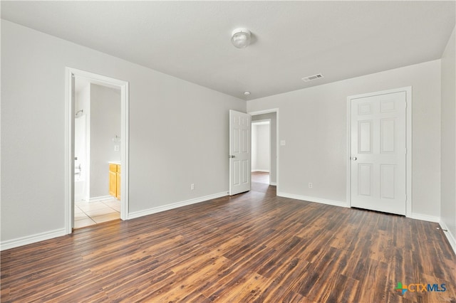 unfurnished bedroom featuring ensuite bathroom and dark hardwood / wood-style floors