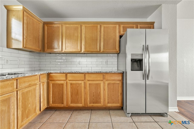 kitchen featuring stainless steel refrigerator with ice dispenser, light stone countertops, light tile patterned flooring, and tasteful backsplash