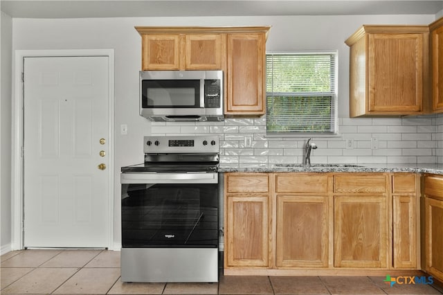 kitchen featuring tasteful backsplash, sink, appliances with stainless steel finishes, light tile patterned floors, and light stone counters