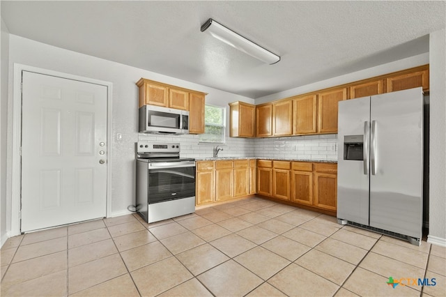 kitchen featuring backsplash, sink, light stone countertops, stainless steel appliances, and light tile patterned floors