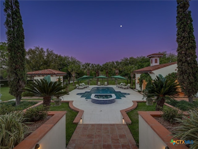 pool at dusk featuring a patio area and an in ground hot tub