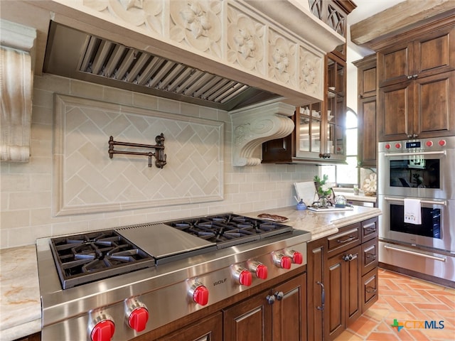 kitchen with light stone countertops, custom exhaust hood, appliances with stainless steel finishes, and tasteful backsplash