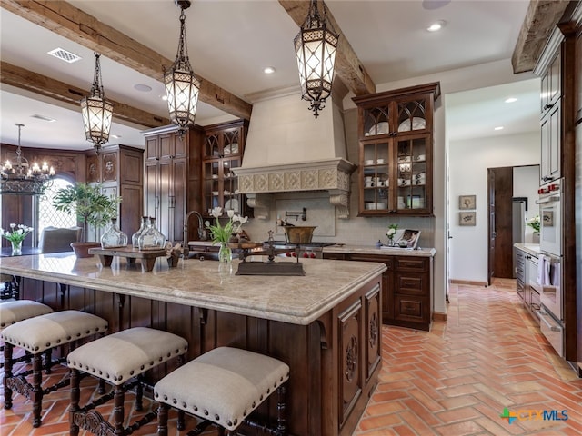 kitchen with tasteful backsplash, a kitchen bar, an inviting chandelier, decorative light fixtures, and a kitchen island with sink