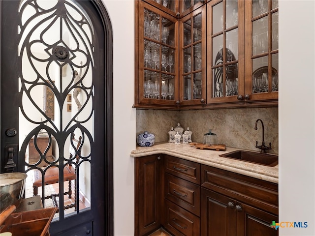 bar featuring decorative backsplash, light stone countertops, sink, and dark brown cabinets