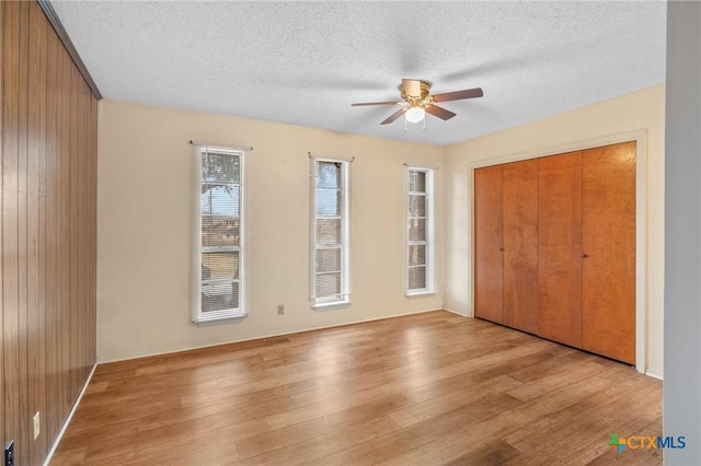 unfurnished bedroom featuring ceiling fan, a textured ceiling, light hardwood / wood-style floors, and a closet