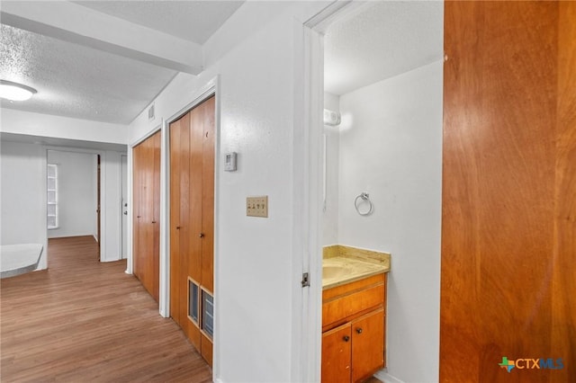 corridor with light wood-type flooring and a textured ceiling