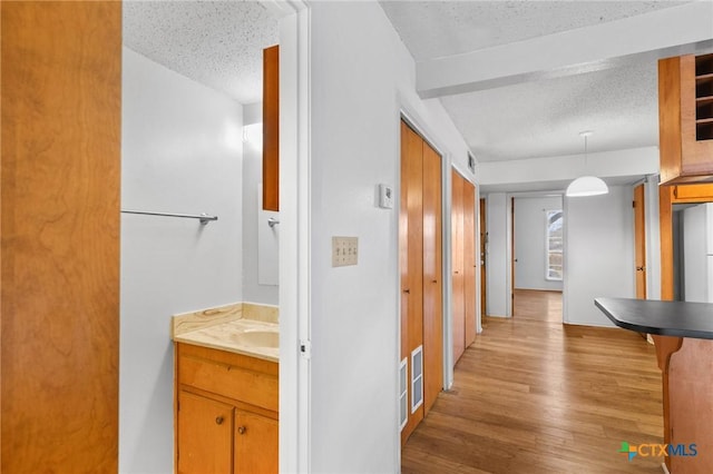 hallway with light wood-type flooring, sink, and a textured ceiling