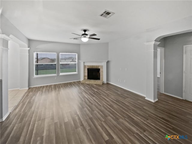 unfurnished living room with ceiling fan, ornate columns, a fireplace, and dark wood-type flooring