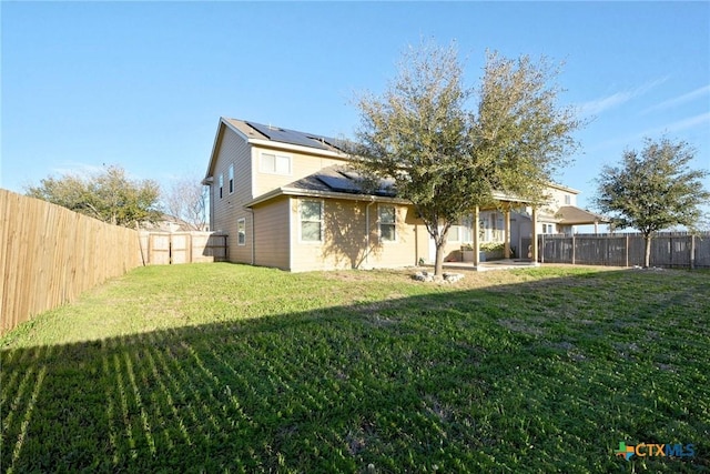 rear view of house with a yard, a patio area, solar panels, and a fenced backyard