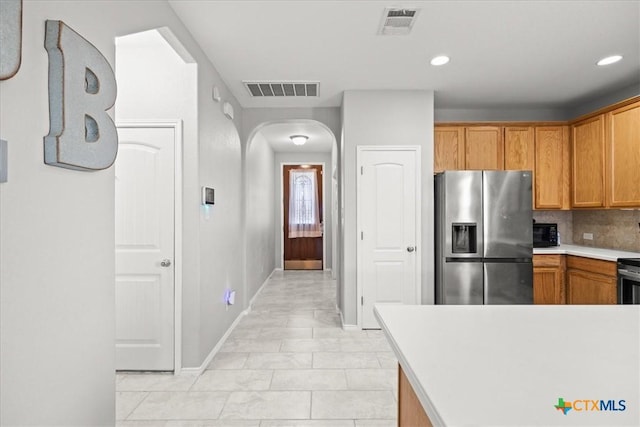 kitchen with light countertops, visible vents, stainless steel refrigerator with ice dispenser, and arched walkways