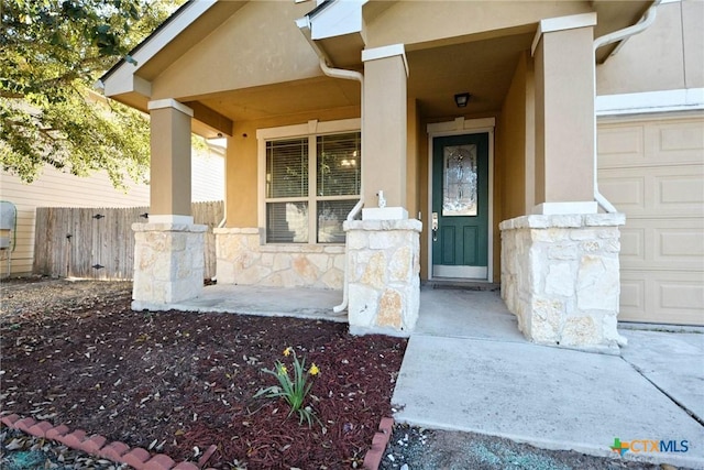 entrance to property featuring stucco siding, stone siding, fence, covered porch, and a garage