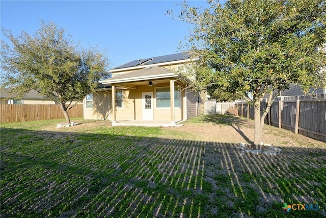 rear view of property featuring solar panels, a fenced backyard, and a lawn