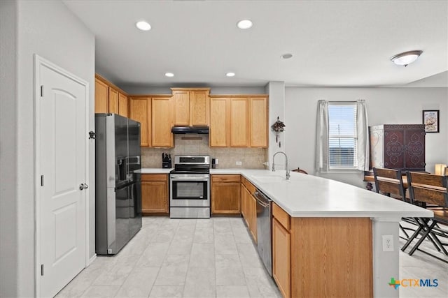 kitchen with under cabinet range hood, light countertops, appliances with stainless steel finishes, a peninsula, and a sink