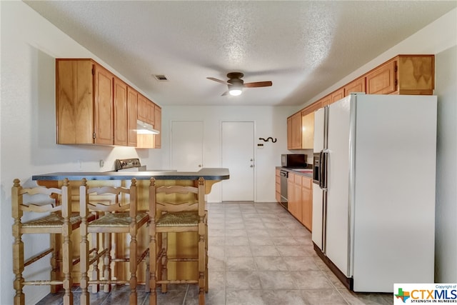 kitchen featuring a breakfast bar, a textured ceiling, white fridge with ice dispenser, and kitchen peninsula