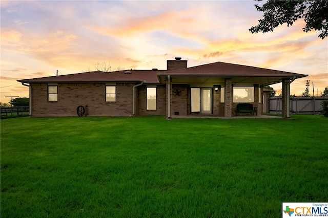 back house at dusk with a lawn and a patio