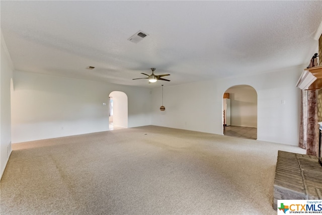 spare room featuring a fireplace, ceiling fan, a textured ceiling, and light colored carpet