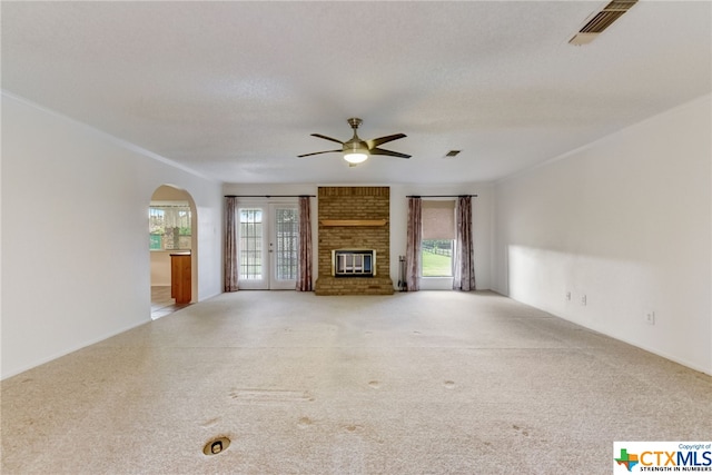 unfurnished living room featuring ceiling fan, a textured ceiling, a healthy amount of sunlight, and a brick fireplace