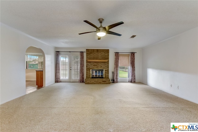 unfurnished living room featuring a brick fireplace, french doors, a textured ceiling, and ceiling fan