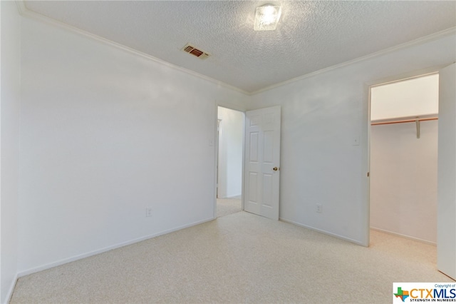 unfurnished bedroom featuring a textured ceiling, a closet, a walk in closet, and ornamental molding