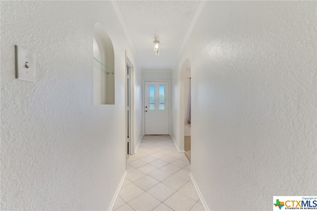 hallway with a textured ceiling, light tile patterned flooring, and crown molding