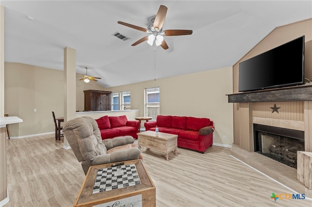 living room featuring vaulted ceiling, ceiling fan, a tiled fireplace, and light hardwood / wood-style floors