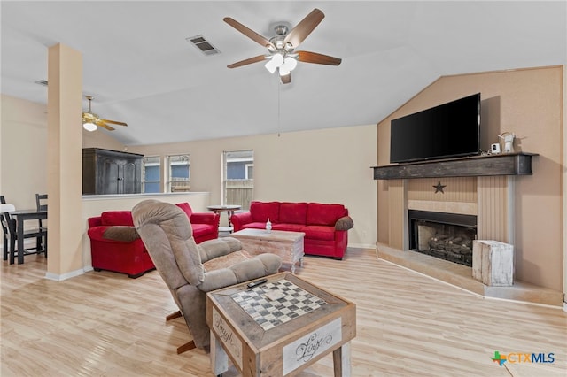 living room featuring a tiled fireplace, light wood-type flooring, and vaulted ceiling