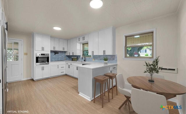 309 E Xavier Ave, Temple, TX 76501 - kitchen with stainless steel oven, a peninsula, light wood-style flooring, backsplash, and recessed lighting
