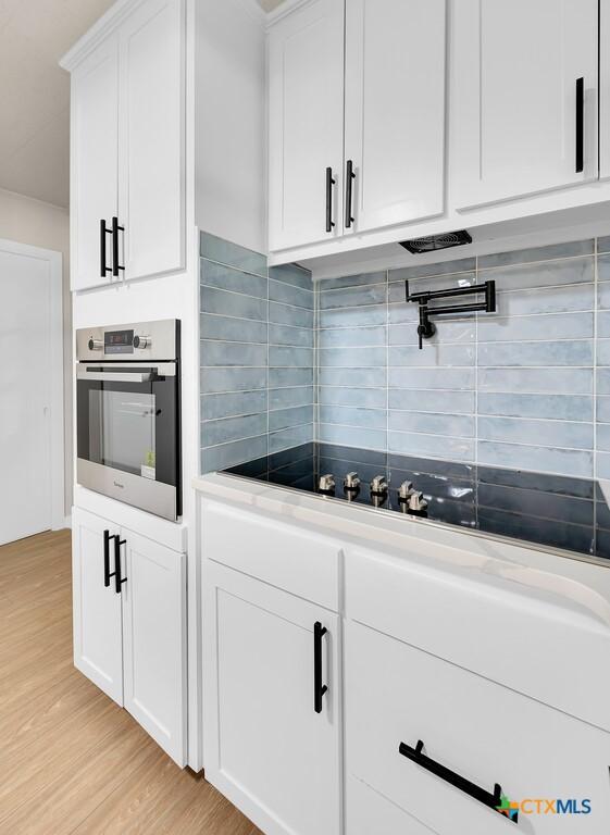 309 E Xavier Ave, Temple, TX 76501 - kitchen with oven, light wood-style flooring, backsplash, white cabinets, and black electric cooktop