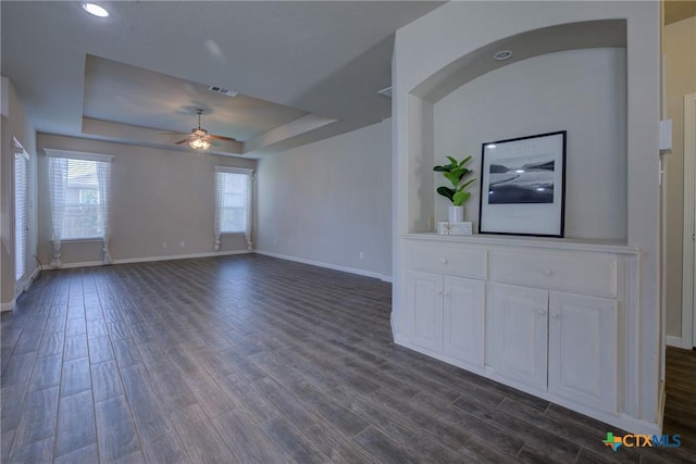 unfurnished living room with visible vents, a tray ceiling, dark wood-style floors, baseboards, and ceiling fan