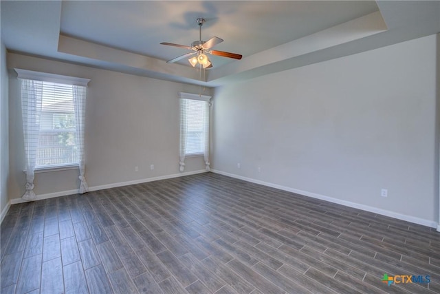 empty room featuring a tray ceiling, dark wood-style floors, baseboards, and ceiling fan