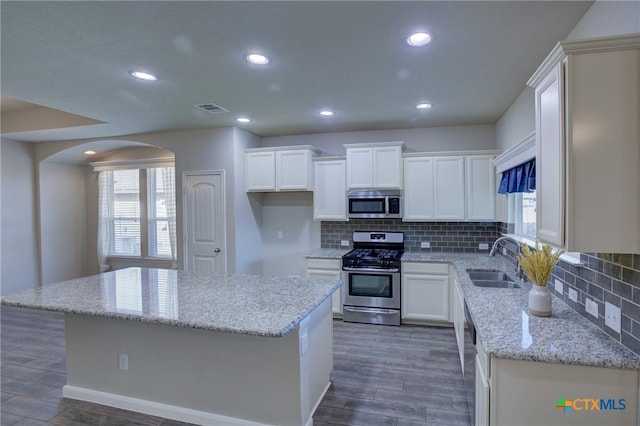 kitchen featuring visible vents, a sink, stainless steel appliances, white cabinetry, and a center island