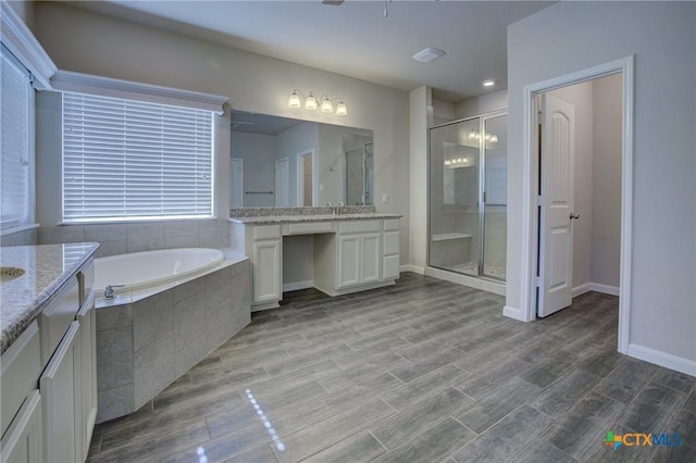 full bathroom featuring baseboards, a garden tub, two vanities, a stall shower, and wood finished floors