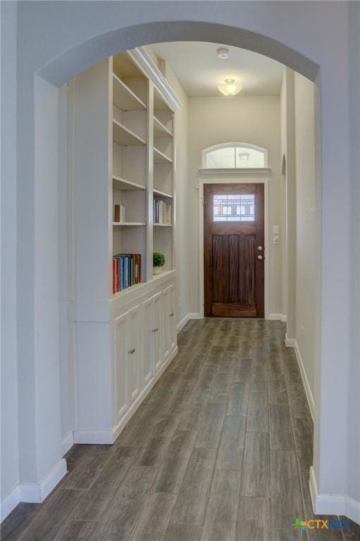 foyer with dark wood finished floors, arched walkways, and baseboards