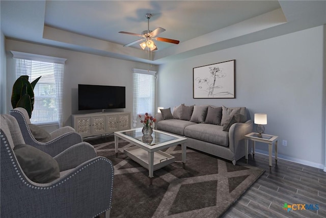 living room with a raised ceiling, a ceiling fan, baseboards, and wood finish floors