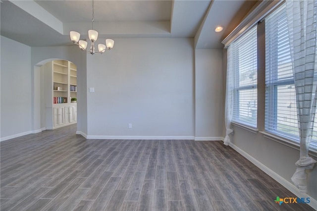 unfurnished room with baseboards, dark wood finished floors, built in features, arched walkways, and a raised ceiling