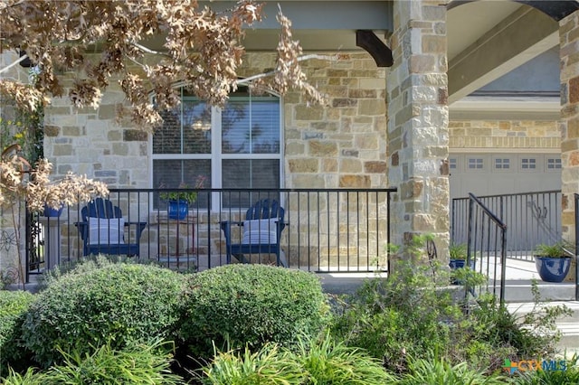 property entrance with a garage, stone siding, and fence