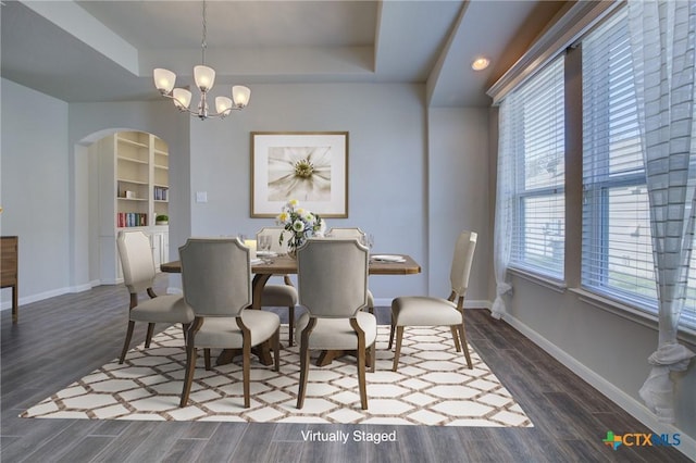 dining space with built in shelves, a raised ceiling, dark wood finished floors, arched walkways, and baseboards