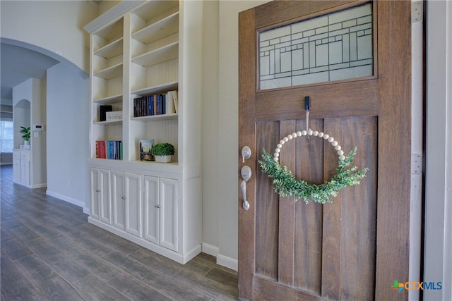 interior space with wood finished floors, arched walkways, and baseboards