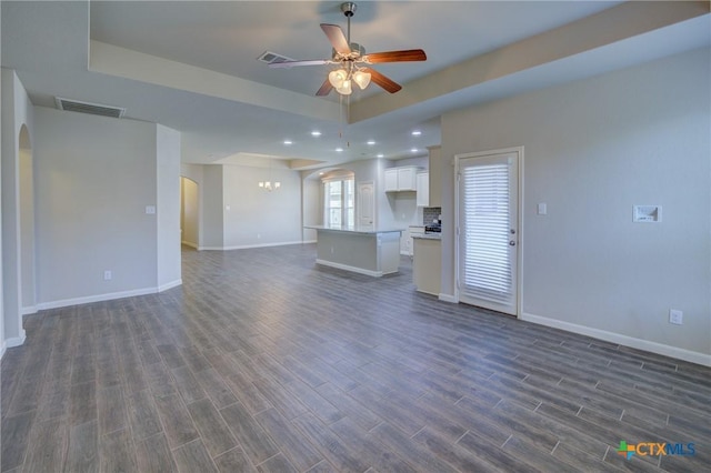 unfurnished living room with dark wood finished floors, a raised ceiling, visible vents, and arched walkways