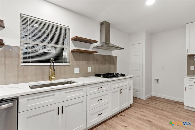 kitchen featuring wall chimney exhaust hood, sink, light stone counters, appliances with stainless steel finishes, and white cabinets