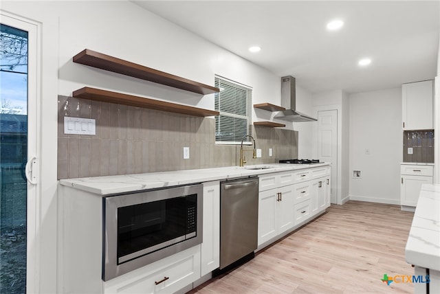 kitchen featuring built in microwave, white cabinetry, light stone counters, light hardwood / wood-style flooring, and wall chimney range hood