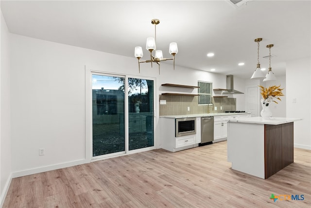 kitchen with appliances with stainless steel finishes, decorative light fixtures, white cabinets, backsplash, and wall chimney exhaust hood