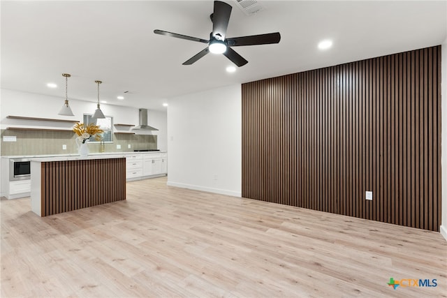 kitchen featuring a kitchen island, white cabinetry, wall chimney range hood, decorative backsplash, and hanging light fixtures