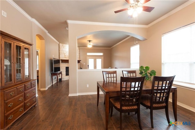 dining room with dark wood-type flooring, ornamental molding, a stone fireplace, and ceiling fan