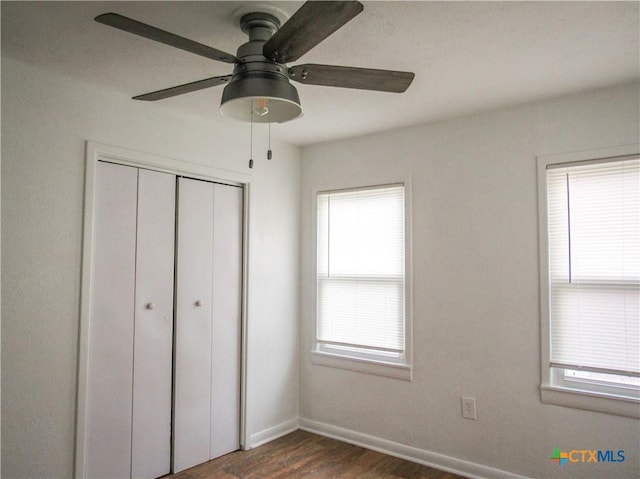 unfurnished bedroom featuring baseboards, ceiling fan, a closet, and dark wood finished floors