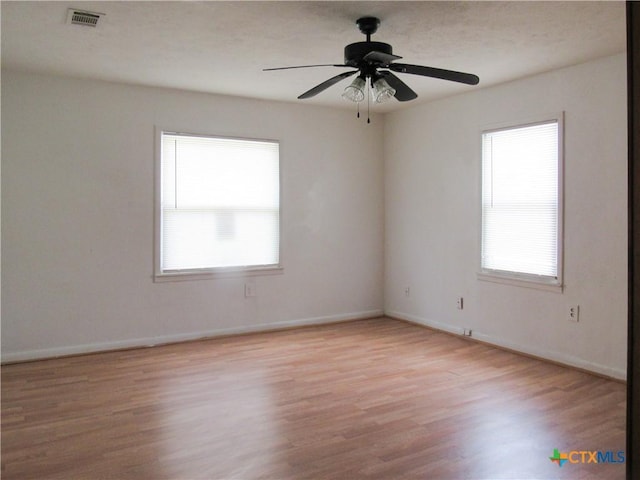 spare room with baseboards, ceiling fan, light wood-style flooring, and visible vents