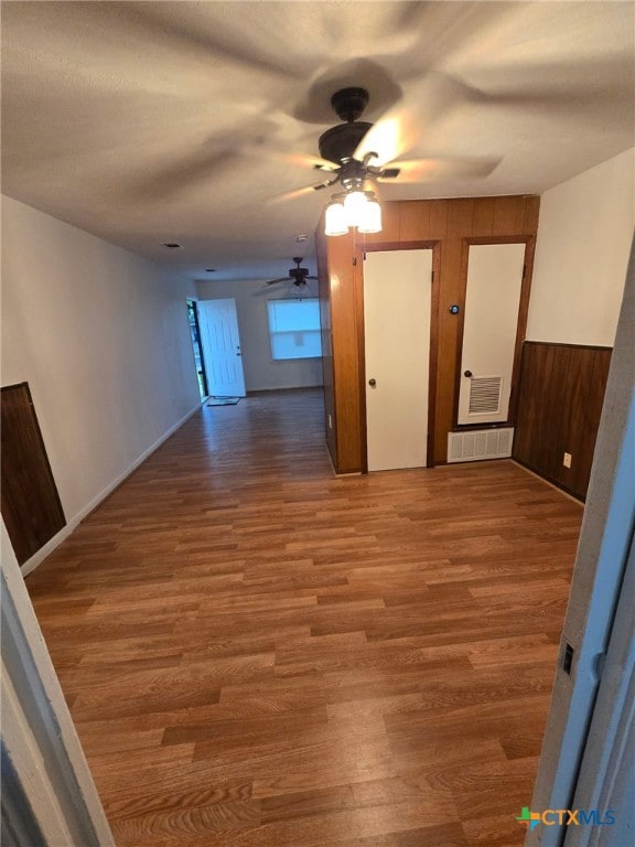 unfurnished room featuring wooden walls, a ceiling fan, wood finished floors, and visible vents
