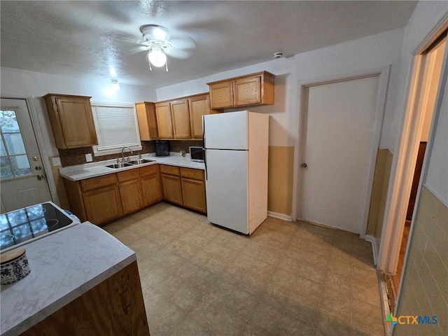 kitchen featuring ceiling fan, brown cabinetry, a sink, light countertops, and freestanding refrigerator